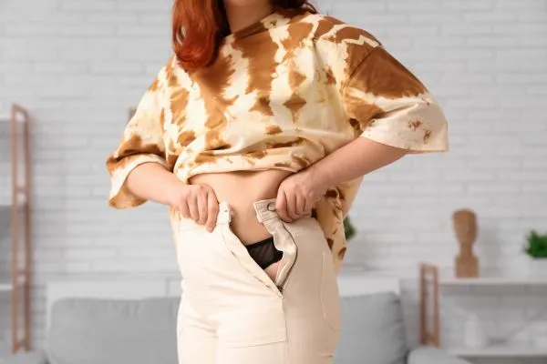 Image of woman trying to do her trousers up after pregnancy weight gain Lichfield